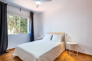 A bedroom with a bed, a nightstand, a lamp, a window with curtains, and a ceiling fan.