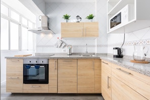 A modern kitchen with wooden cabinets, a built-in oven, a microwave, and a coffee maker.