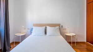 A neatly made bed with white linens, two bedside tables with lamps, and a wooden headboard. - Apartamento Residencial Limonar with A/C & Wi-Fi (Málaga)