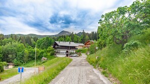 A rural road leading to a house with a sloped roof, surrounded by greenery and a mountain in the background. - Apartment at "Chalet Jade" with Mountain Views, Balcony, and Wi-Fi (Saint-Gervais-les-Bains)