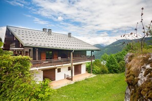 A modern house with a sloped roof, wooden balcony, and a view of green hills.