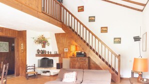 A living room with a wooden staircase, a sofa, a coffee table, and a television. - Apartment at "Chalet Jade" with Mountain Views, Balcony, and Wi-Fi (Saint-Gervais-les-Bains)
