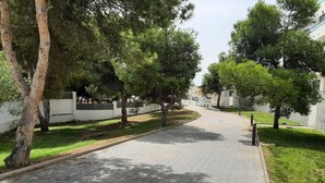 A paved pathway flanked by trees and a white wall, leading to a building. - Apartment 'Alegria' near the Beach with Shared Pool (Garrucha)