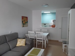 Een ruimtelijke woonkamer met een bank, eettafel, stoelen, een keuken met kasten en een schilderij aan de muur.