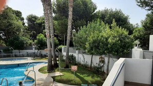An outdoor swimming pool with a tiled deck, surrounded by trees and a white wall. - Apartment 'Alegria' near the Beach with Shared Pool (Garrucha)