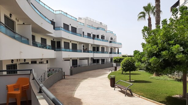 A multi-story building with balconies, a paved walkway, outdoor seating, and greenery. - Apartment 'Alegria' near the Beach with Shared Pool (Garrucha)
