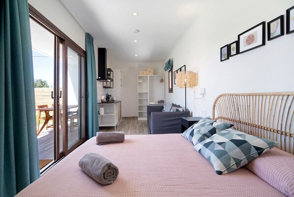 Une chambre à coucher comprenant un lit, des oreillers, une table de chevet, une armoire et une vue sur l’extérieur, accessible par une porte coulissante.