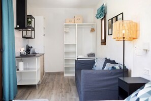 Une chambre moderne avec un canapé gris, une armoire blanche, une petite table avec une lampe et un rideau bleu.
