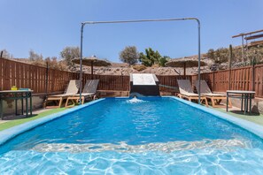 A swimming pool with a slide, surrounded by wooden fences, and a few lounge chairs.