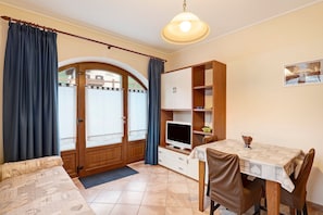 A room with a bed, a TV, a dining table with chairs, a cabinet, and a door leading outside. - Apartment 'Greta Baita Mauri' with Balcony & Wi-Fi (Sant'Anna)
