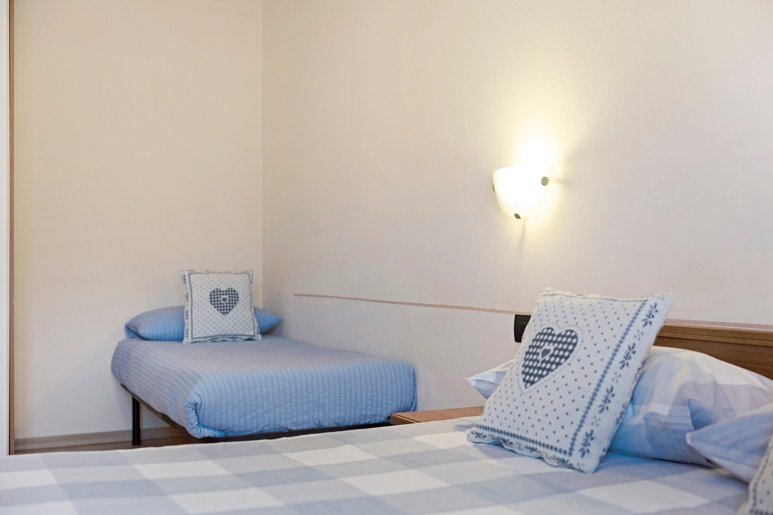 Une chambre avec deux lits, une lampe fixée au mur et des coussins à motifs de cœurs.