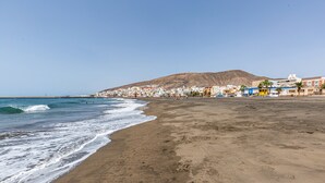 A beach with a clear view of the ocean, a sandy shore, and a town with buildings in the background. - Holiday Apartment "La Fortaleza - Casa La Fuentita - Adults Only" with Mountain Views (La Fuentita)