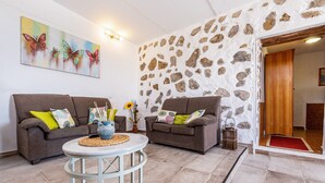 A living room with two sofas, a round table, a painting, and a stone wall. - Holiday Apartment "La Fortaleza - Casa La Fuentita - Adults Only" with Mountain Views (La Fuentita)