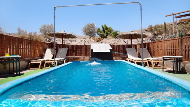 A rectangular swimming pool with a slide, surrounded by wooden fences, and equipped with lounge chairs and tables. - Holiday Home 'Esencia Eco-rústico - Adults Only' with Shared Pool and Garden (La Fuentita)