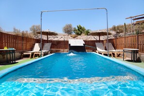 Ein rechteckiger Swimmingpool mit Rutsche, umgeben von Holzzaun, mit Liegestühlen und Tischen ausgestattet.