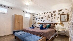 A bedroom with a bed, a wooden wardrobe, a bench, a nightstand, and a stone-patterned wall. - Holiday Home 'Esencia Eco-rústico - Adults Only' with Shared Pool and Garden (La Fuentita)
