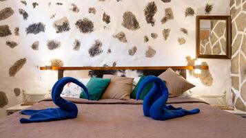 Un dormitorio con pared de piedra, estructura de cama de madera y cama con colcha marrón y almohadas azules.
