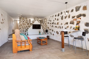 Ein Zimmer mit Steinwand, einem Holzsofa, einem Fernseher, einem Tisch mit Stühlen und einer kleinen Pflanze.