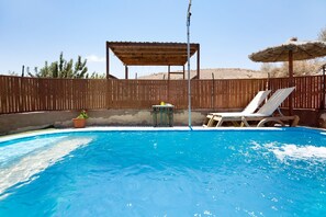 Una piscina con muelle de madera, sillas de descanso y un pérgola.