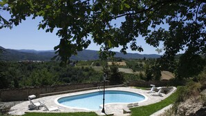 A swimming pool with lounge chairs, surrounded by a stone deck and a view of a mountainous landscape. - Erica / Cornflower two-room apartment (Guardia)
