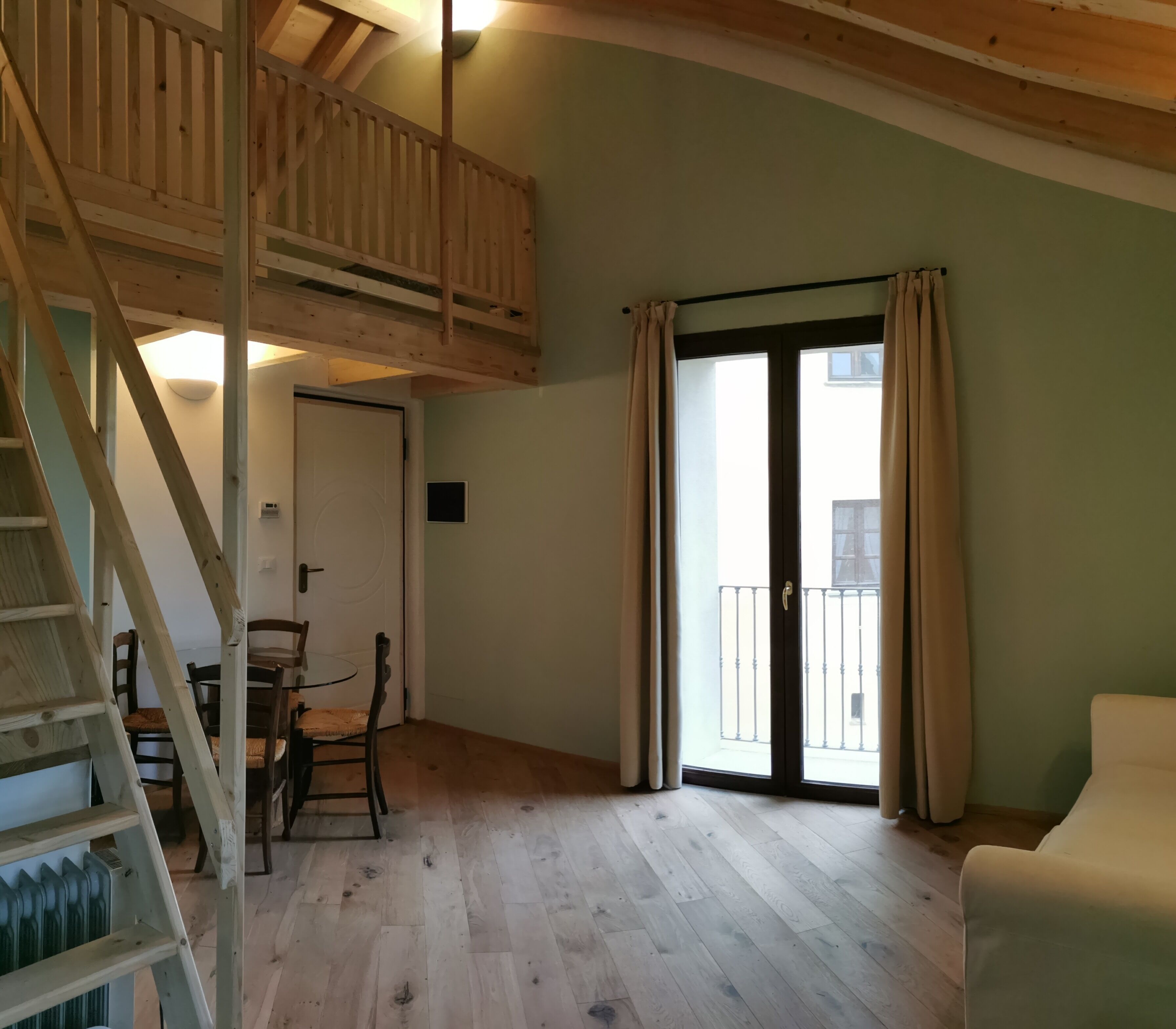 Ein geräumiges Zimmer mit einer Holztreppe, einem Essbereich mit Stühlen und einer Glastür, die auf einen Balkon führt.