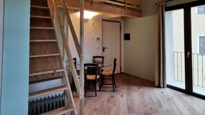 A room with a wooden staircase, a dining area with a table and chairs, and a large sliding glass door leading to an outdoor balcony. - Erica / Cornflower two-room apartment (Guardia)