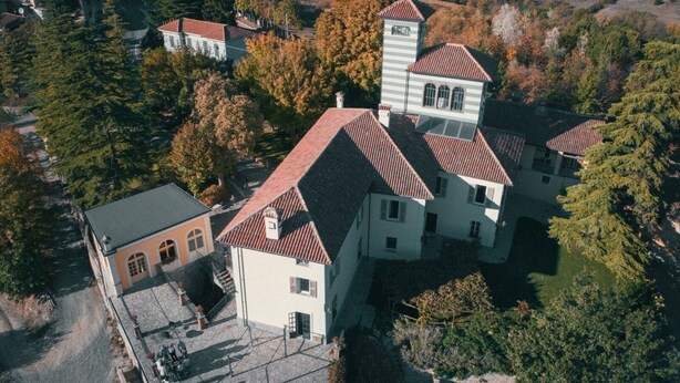 A large, multi-story building with a red-tiled roof, surrounded by trees and other buildings. - Erica / Cornflower two-room apartment (Guardia)
