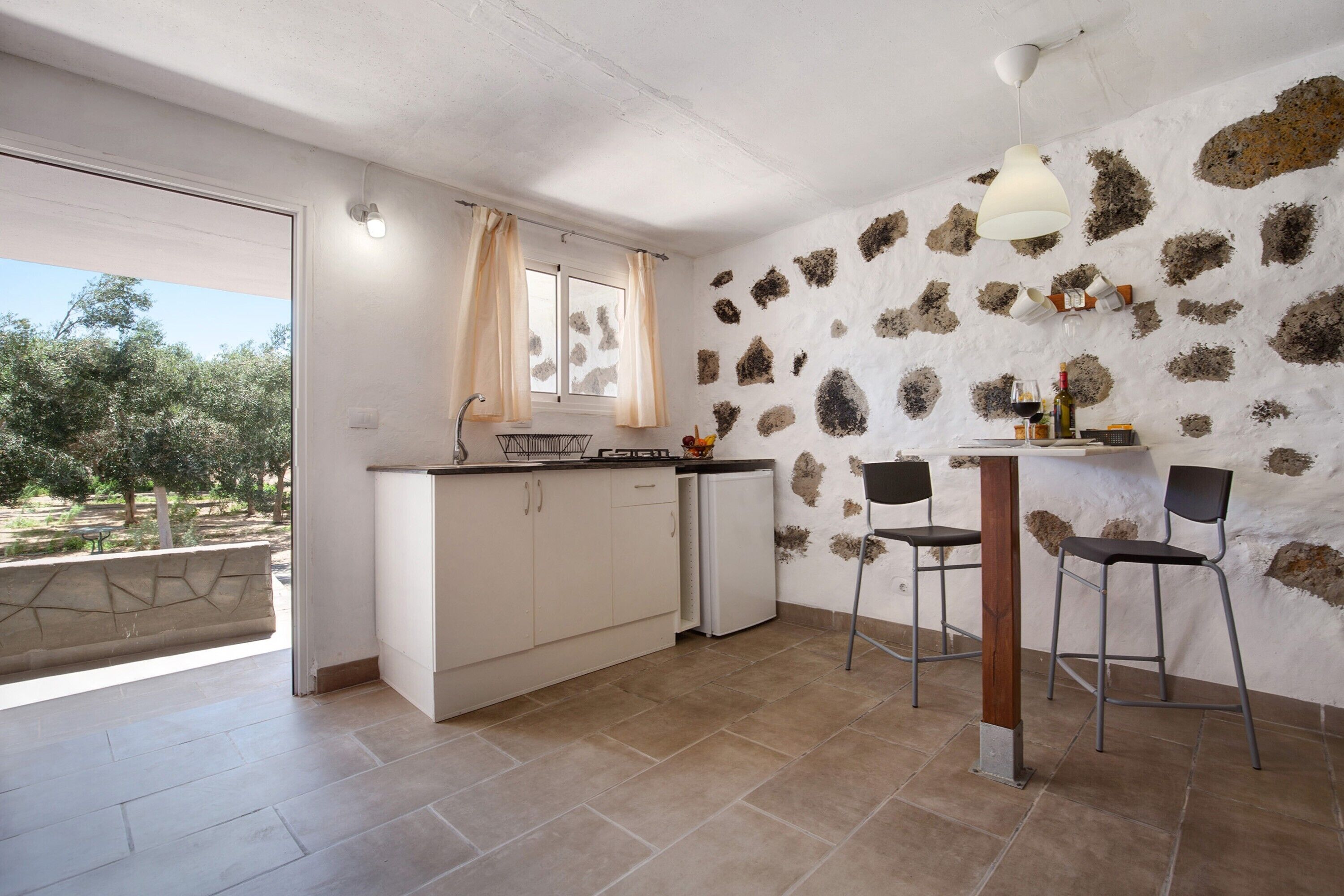 A kitchen with a stone wall, a dining area with two chairs, and a view of trees through a glass door.