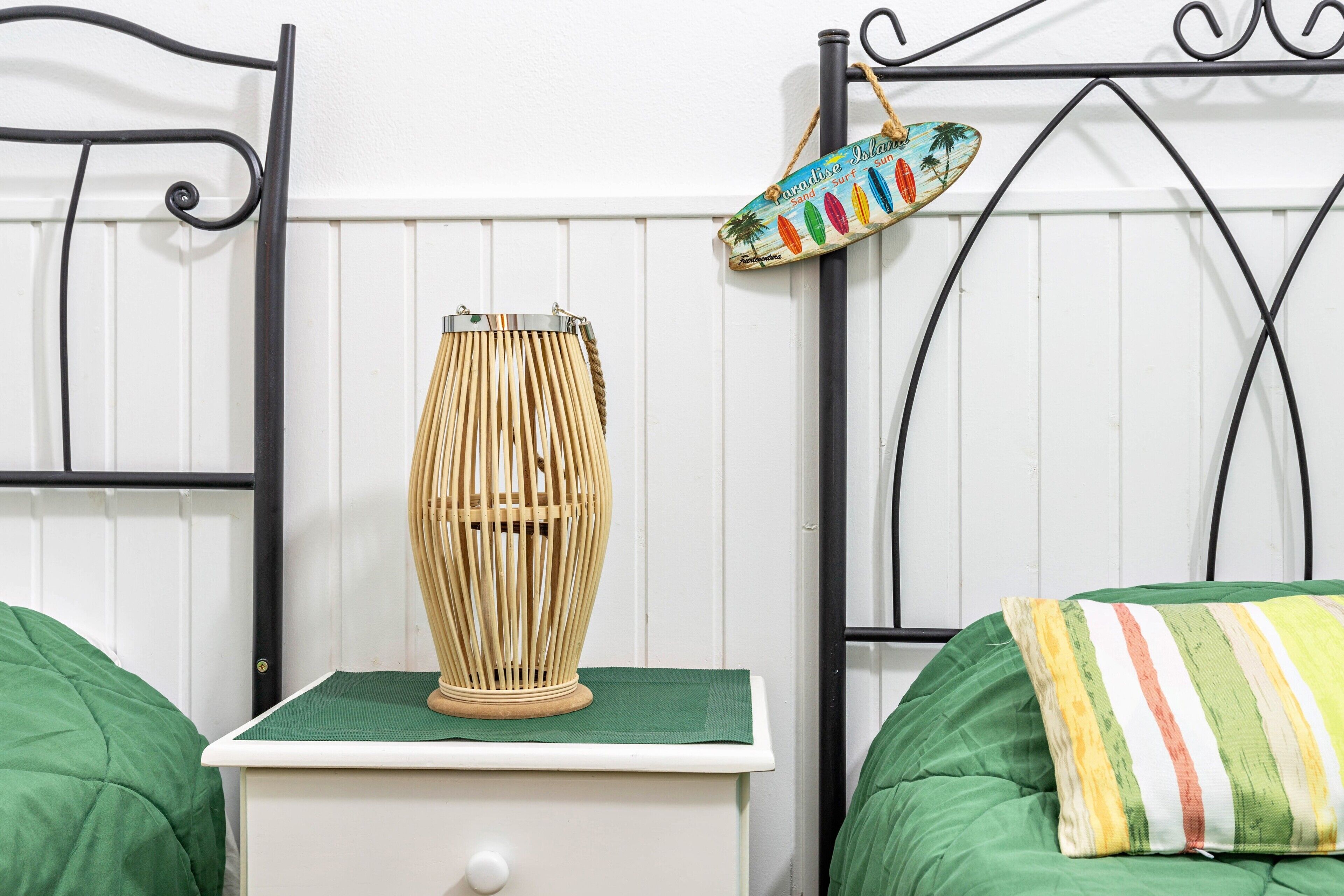A bed with green bedding, a bedside table with a lamp, and a wall-mounted sign.