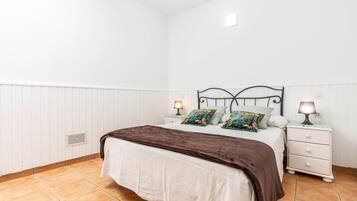 Un dormitorio con una cama, dos mesitas de noche con lámparas, un calentador y una pared blanca.