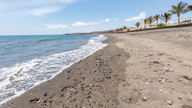 Ein Strand mit felsigem Ufer, Palmen und blauem Himmel.