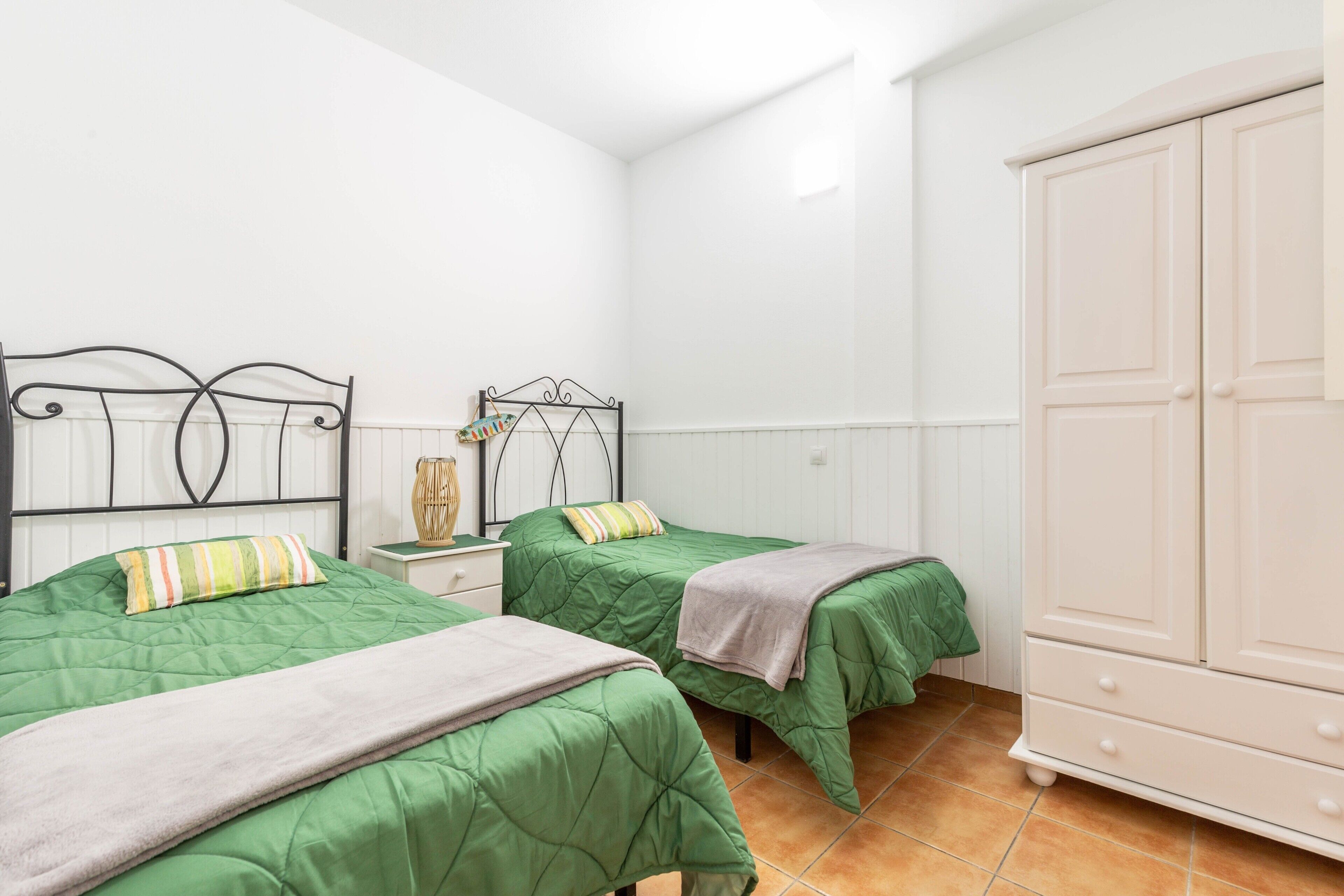 Une chambre avec deux lits, une table de chevet, une armoire et un radiateur.
