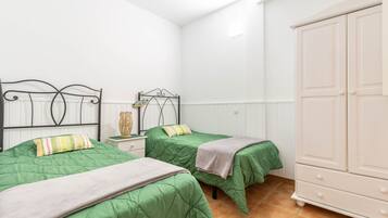 Une chambre avec deux lits, une table de chevet, une armoire et un radiateur.