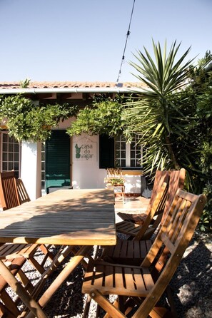 A wooden table and chairs in a sunny outdoor area with a green door and a sign that reads 'casa do vagar'.