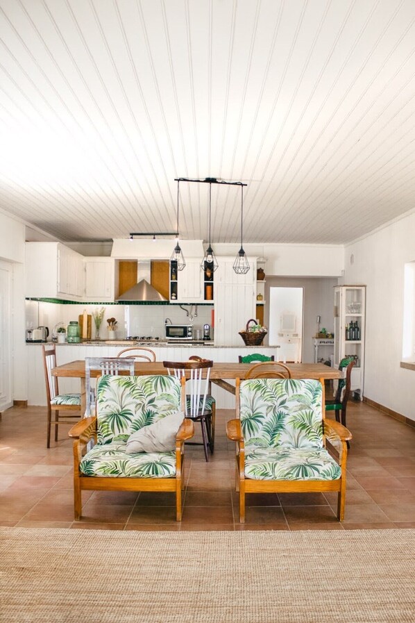 A spacious kitchen with white cabinets, a wooden dining table, and two chairs with tropical upholstery.