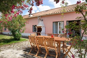 Un bâtiment rose avec un toit en tuiles, une table et des chaises en bois, et une cheminée.