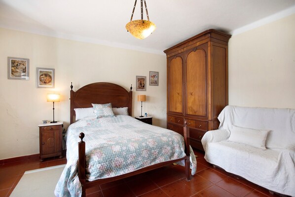 A bedroom with a wooden bed, a white sofa, a wooden wardrobe, and two bedside lamps.