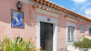 Un edificio rosa con techo de tejas, una puerta con la etiqueta 'AL' y un cartel con el número '47'.