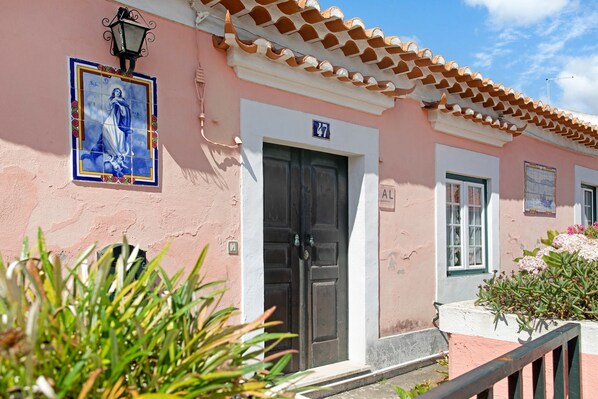 A pink building with a tiled roof, a door labeled 'AL', and a sign with the number '47'.