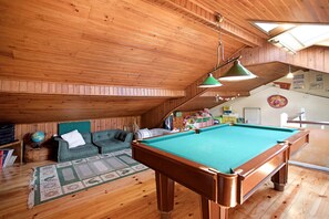 Una habitació amb panells de fusta, una taula de billar, un sofà verd i un glob dins un tamboret de fusta.