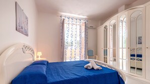 Ein Schlafzimmer mit einem Bett, einem Nachttisch, einem Stuhl, einem Kleiderschrank und einem Fenster mit Vorhängen.