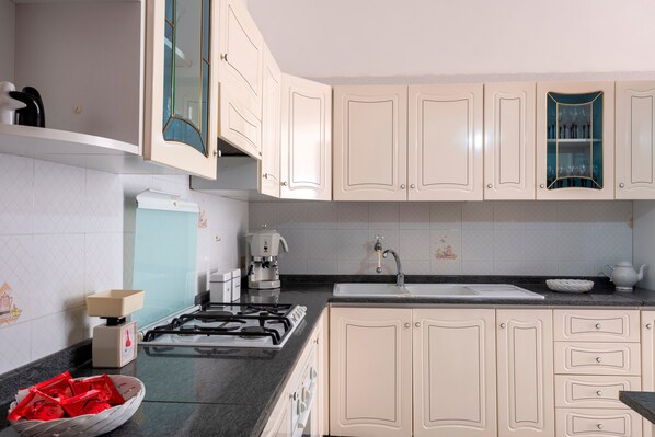 A kitchen with white cabinets, a gas stove, a coffee maker, and a sink.