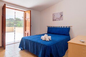A bedroom with a bed, a wooden nightstand, a painting on the wall, and a sliding glass door leading to an outdoor balcony.