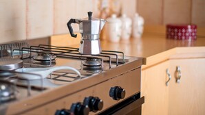 Une cuisine équipée d’une cuisinière à gaz, d’une cafetière et d’un récipient rouge posé sur le plan de travail.