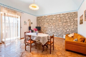 Un espace repas comprenant une table, des chaises, un canapé, un mur en pierre et un téléviseur.