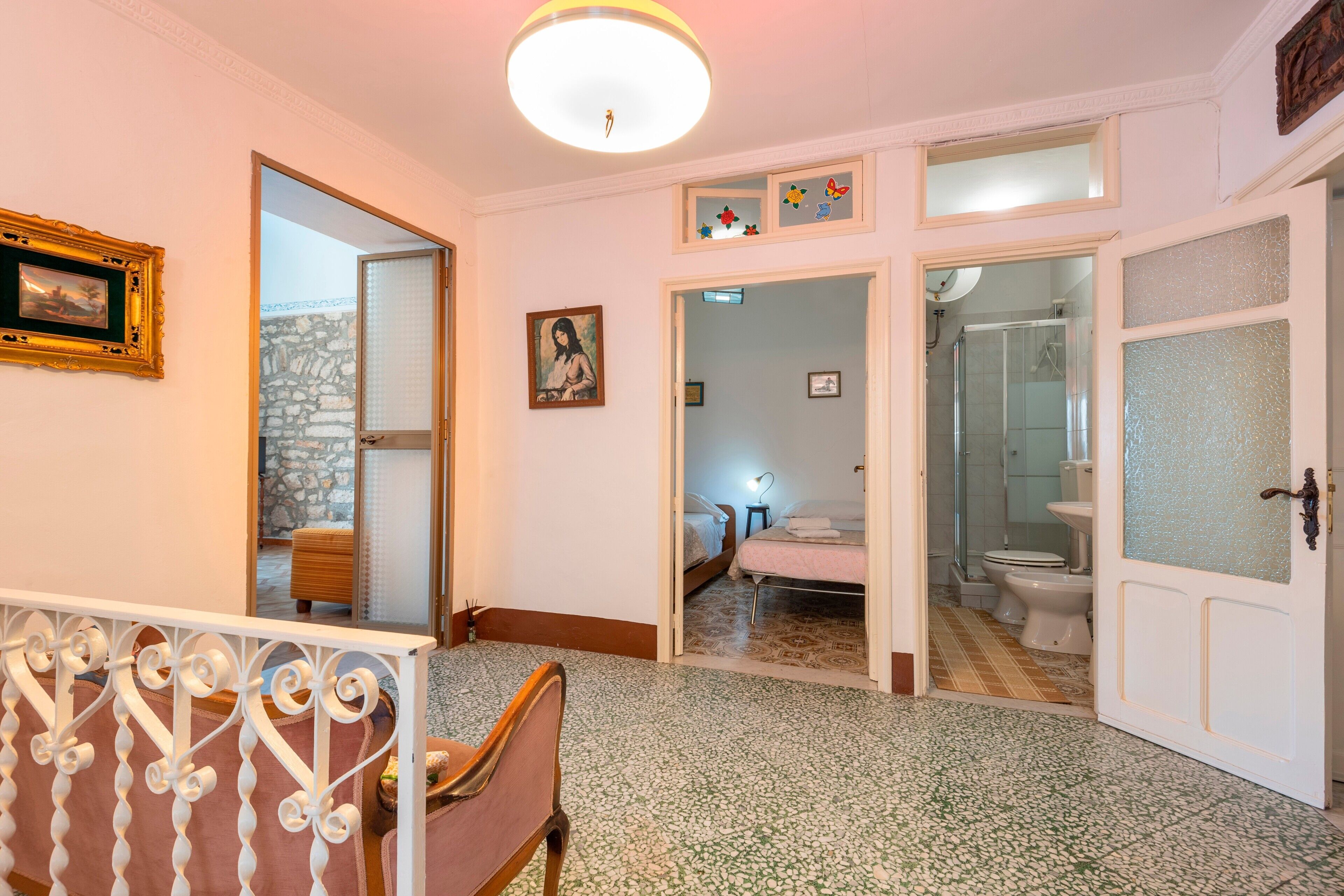 A hotel room with a bed, a chair, a bathroom with a shower, and a visible corridor.