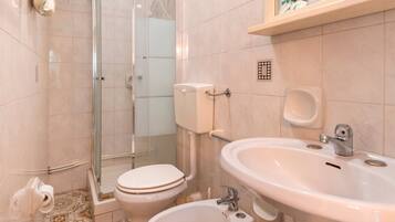 A bathroom with a toilet, bidet, sink, and shower area.