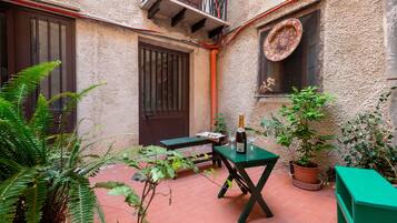 A courtyard with a green table, a potted plant, and a bottle of wine.