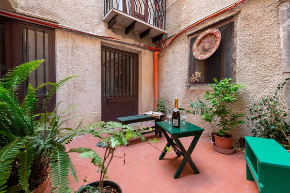 A courtyard with a green table, a potted plant, and a bottle of wine.