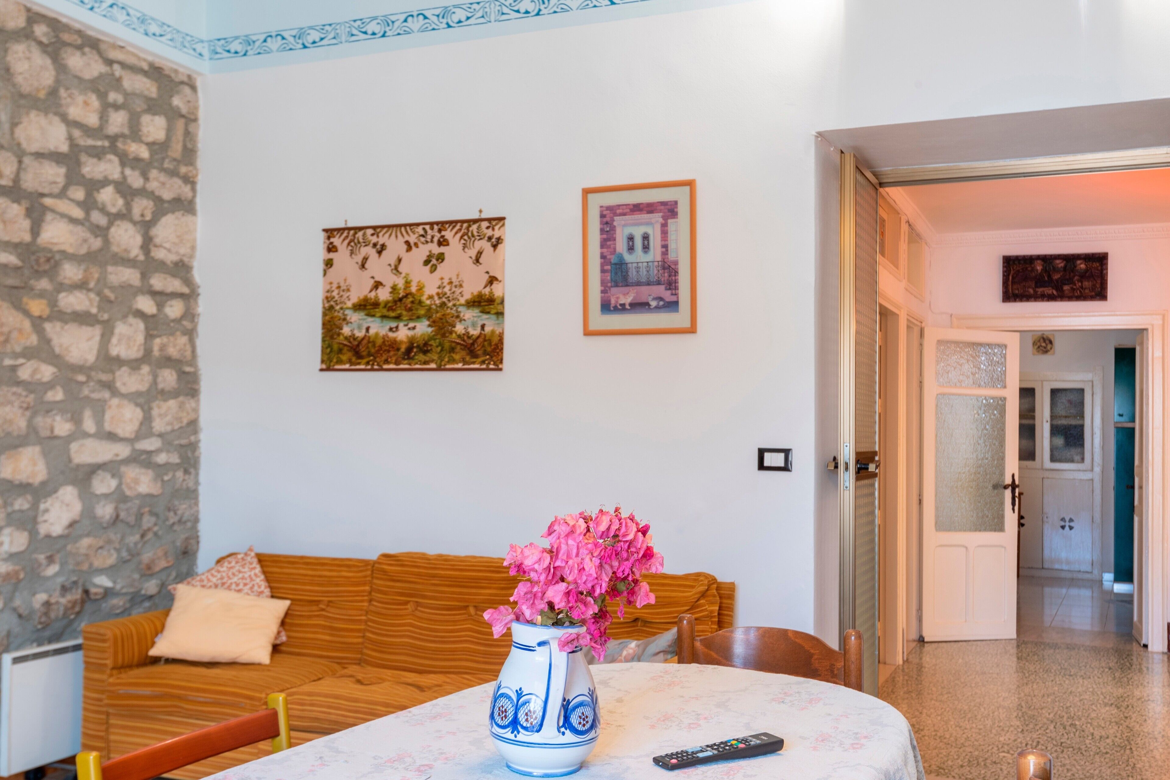 Una habitación con pared de piedra, sofá de madera, una mesa con un jarrón de flores y cuadros en la pared.